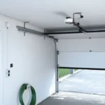 Close-up of a garage door mechanism showing the metal tracks and springs. The door has white panels, and a red tag is attached to the track. The image is time-stamped in the bottom right corner at 8:29 PM. and this image belongs to article 'How to Make Perpendicular Garage Door Horizontal Tracks'