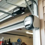 A garage door partially open with a Chamberlain Liftmaster opener mounted on the side. The interior shows storage items. A decorative horseshoe is attached to the wall near the opener.